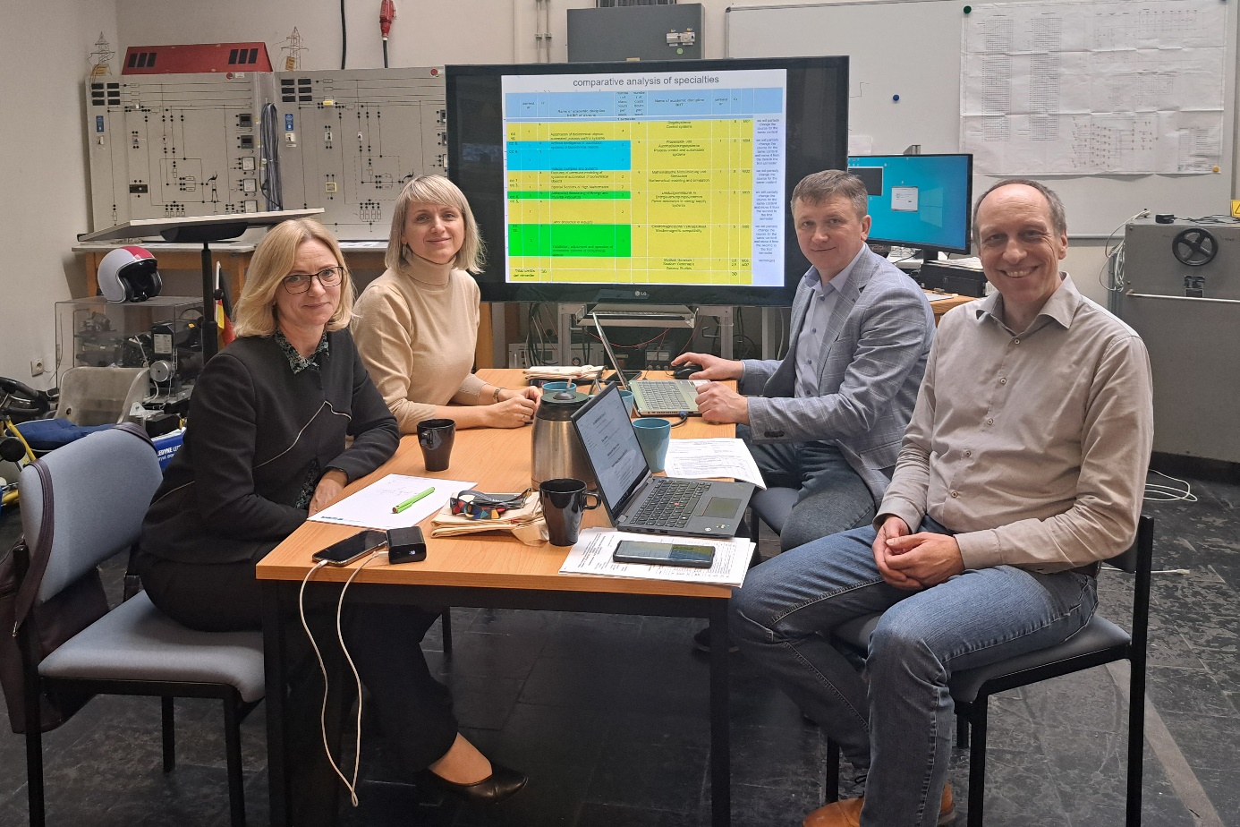 Vier Personen sitzen in einem technischen Labor um einen Tisch herum